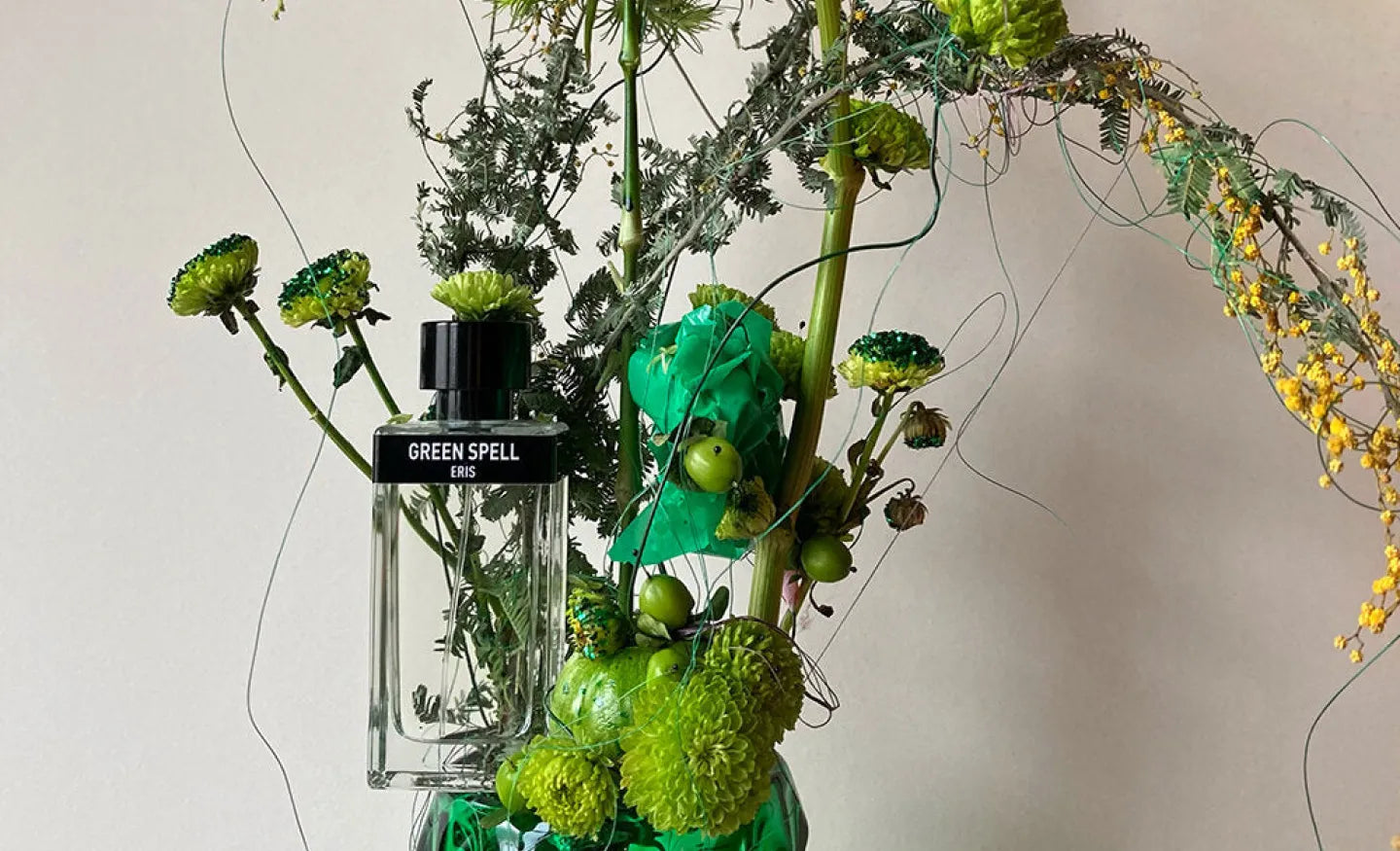 A bottle of ERIS Parfums fragrance Green Spell amid a green Ikebana floral arrangement
