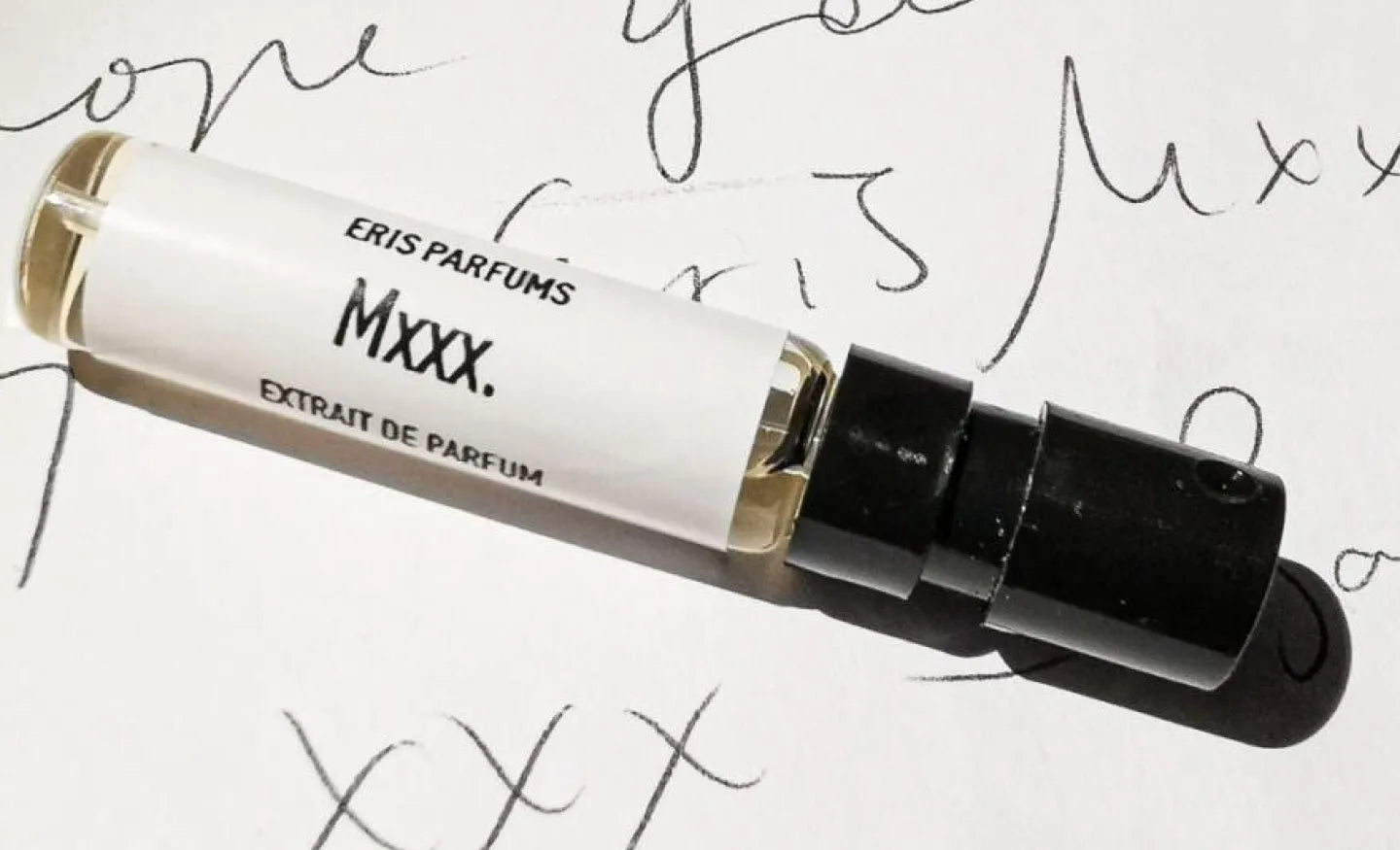 A sample spray bottle of ERIS Parfums Mxxx. eau de parfum on a white paper background with obscured text written on it